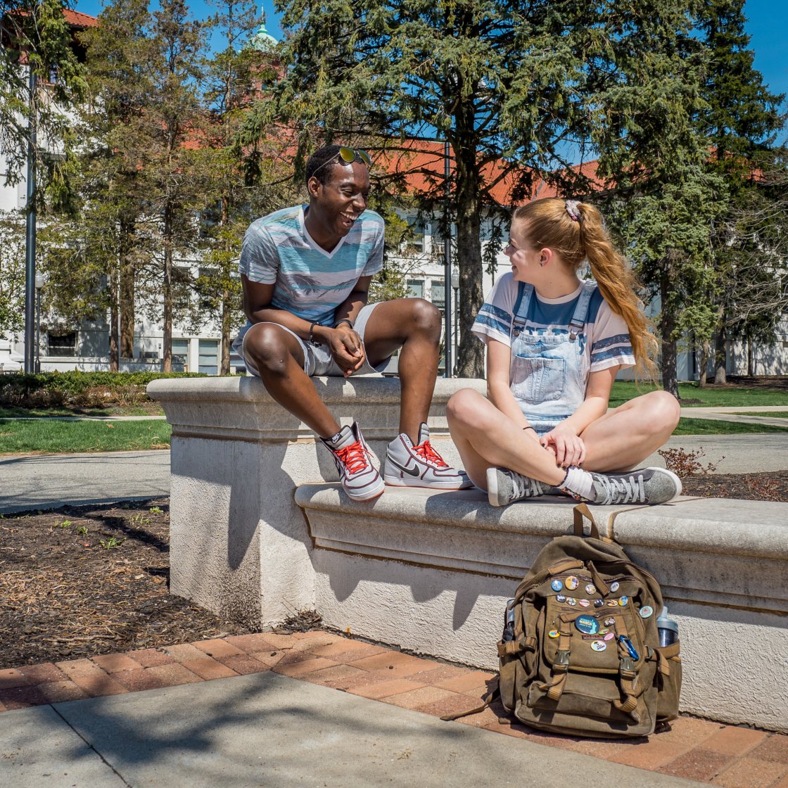 Two students sitting on campus engaged in a lively discussion.