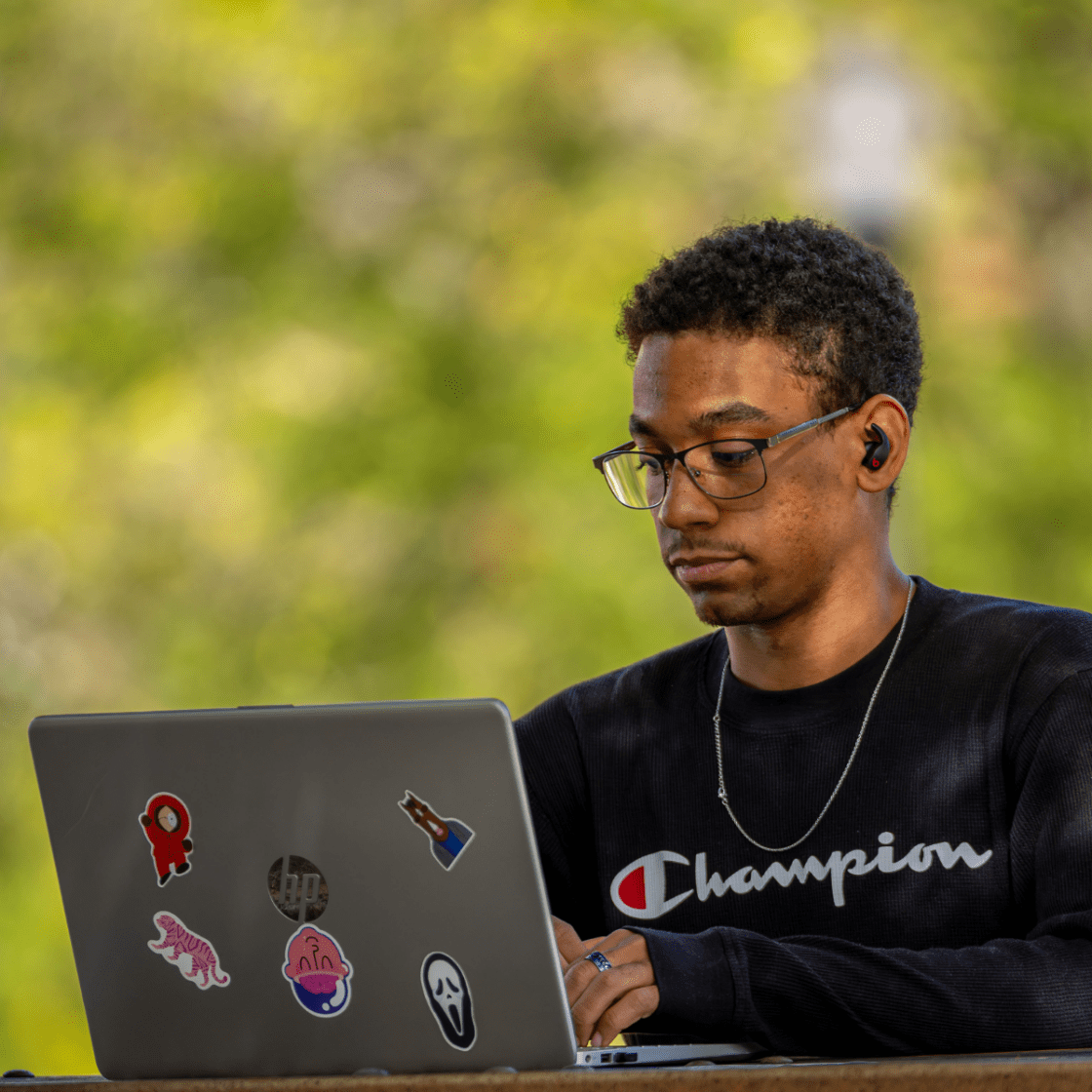 A student sits outside working on their laptop.