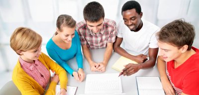 A diverse gorup of people  sit around a table and look at a laptop screen