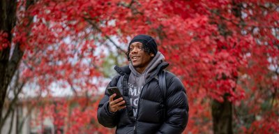 student on phone in front of red trees
