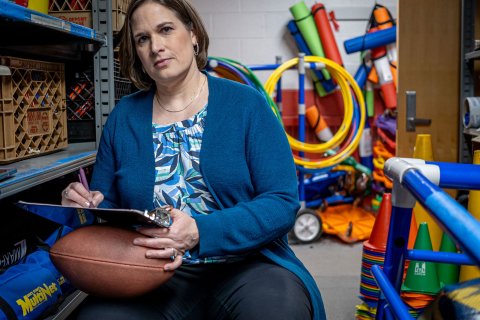 Kinesiology Professor Melissa Alexander is seated, holding a clipboard and football.