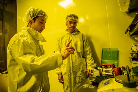 Two men in lab coats under the yellow light of the lab.