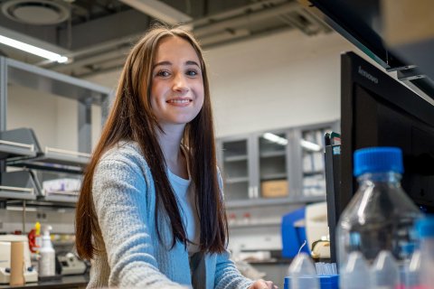 A female student smiles at a computer in a science lab.