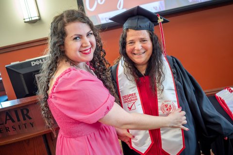 A young woman adjusts her mother's graduation stole.