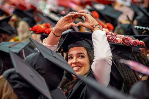 A graduate smiles and holds up their hands in the shape of a heart
