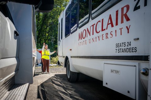 Woman in between two Montclair University buses signaling. 