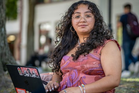 Sara Flores sitting on campus with her laptop open.