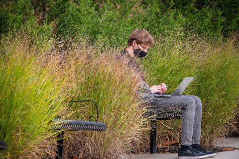 Male sitting outside on a bench, wearing a mask