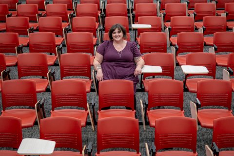 A student sits in the center of a lecture hall filled with red chairs.