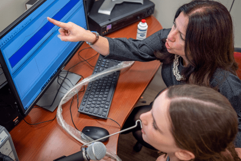 Professor and student in speech lab inspecting an audio waveform on a computer monitor