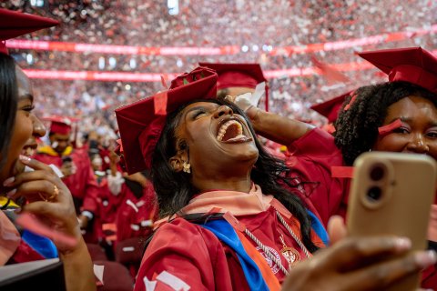 master's graduate student in red cap and gown smiling with confetti falling around them