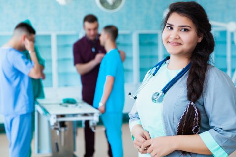 Woman in medical attire, stethoscope around her neck and her colleauges in the background.