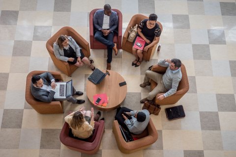 Seven graduate students collaborating while seated in a circle with laptops and papers