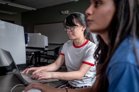 Two students in a lab, one using a computer
