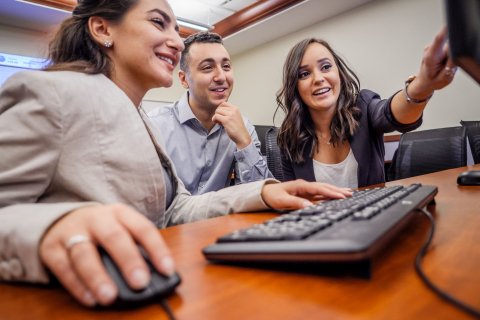 A group of three students sit around a computer and study the screen