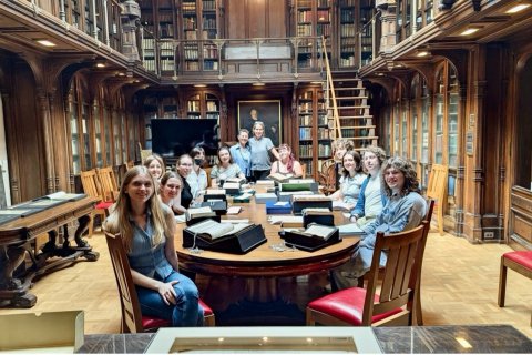 A group of students sit around a long table in a large, wood-paneled library.