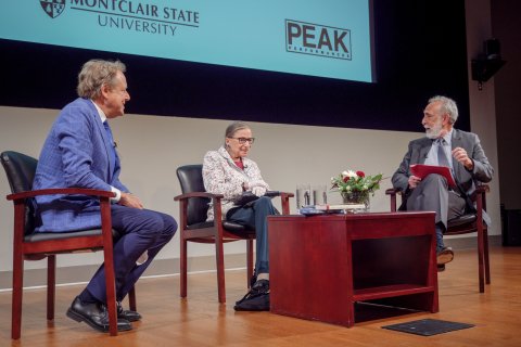 Ruth Bader Ginsburg on stage with two other men discussing.