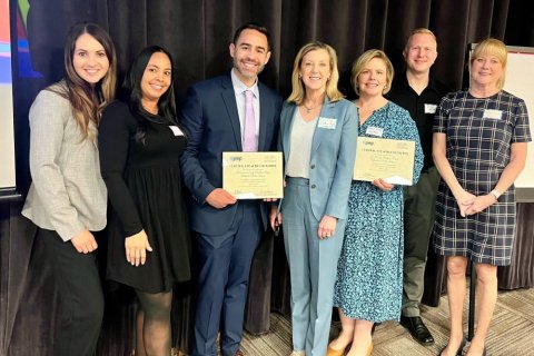 Seven professionals standing side by side holding certificates