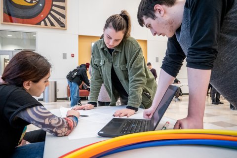 Three students discussing around a table with a laptop and hulahoops joops
