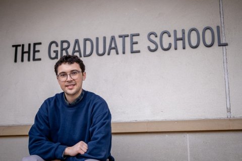 Student sitting in front of The Graduate School sign