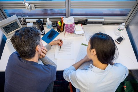 writing consultation session with student and faculty at a desk reading and reviewing a paper