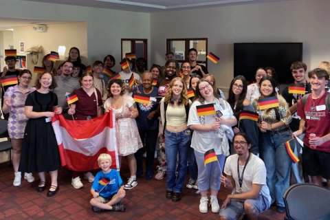 A large group of people stand together and hold small German flags while two people  hold a large Austrian flag