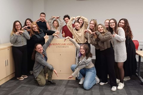 A group of people pose around a podium and point to the "Montclair State University" logo on it