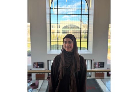 A woman wearing a hijab poses for a headshot in front of a window 