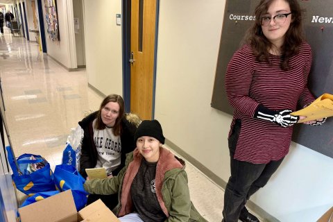 Three college students pose with a pile of bags of donated books 