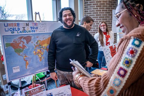 A man stands in front of a map at a booth and smiles at a visitor