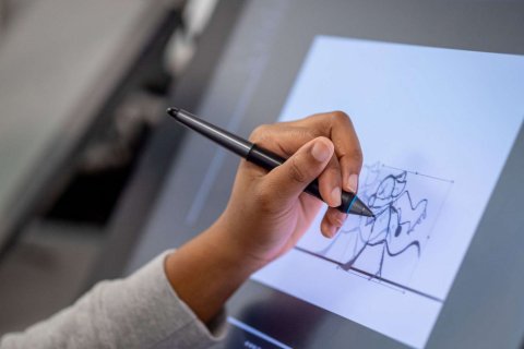 A hand holds a pen and draws a sketch on a piece of paper on a light table