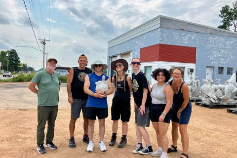 A group of 7 people post in front of a store front, one holds a concrete turtle statue