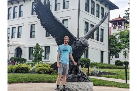 A college student stands in front of bronze statue of a Red Hawk
