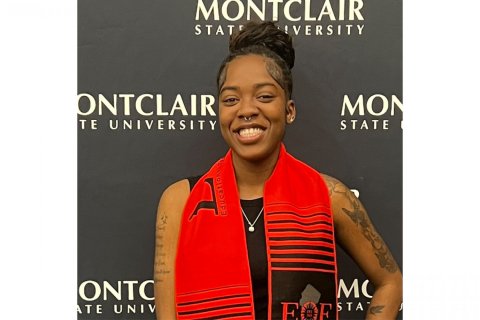 A college student poses in front of a school-branded backdrop
