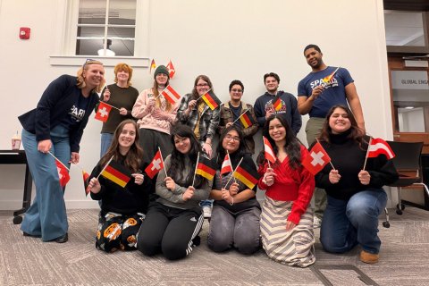 A group of students pose for a group photo holding German, Swiss, and Austrian flags
