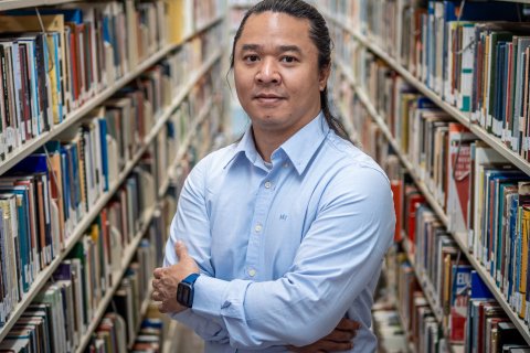 Kaung Hla Zan stands between two long shelves of books in a library.