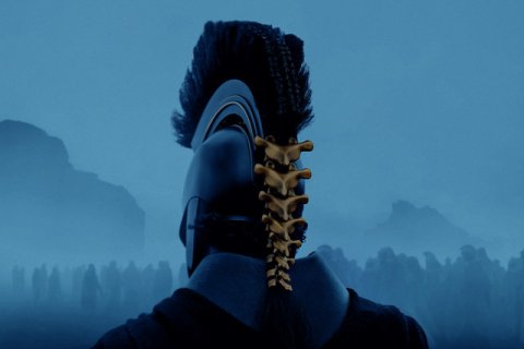 Man in helmet with gold spine on the back of his head riding into war. It is dark and foggy and you can see the outlines of the mountains ahead. 