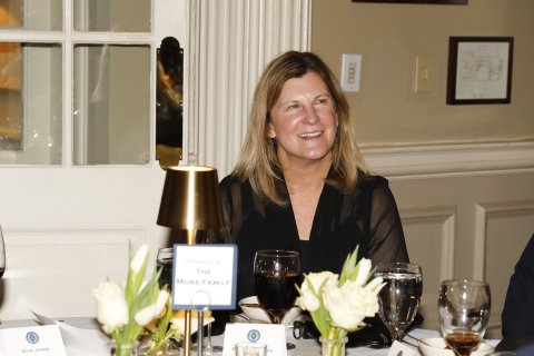A woman with long dirty blonde hair sitting at a table. She is smiling and happy.