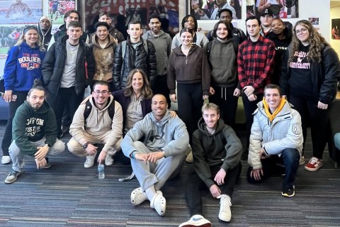 Students in two rows, some sitting and others standing, smiling and looking relaxed.