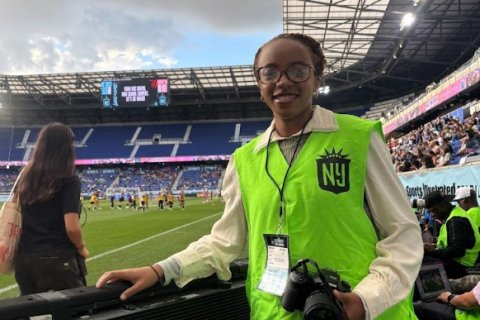 Student in light green Gotham FC vest holding camera.