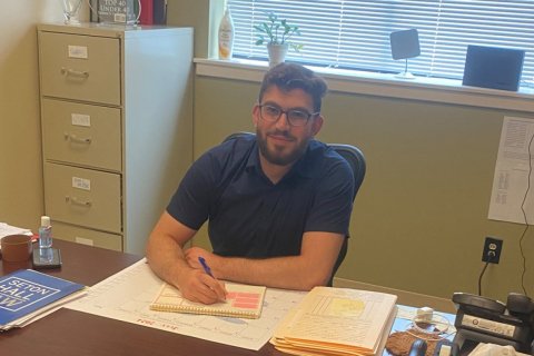 a man sits behind a desk in an office and writes into a notebook