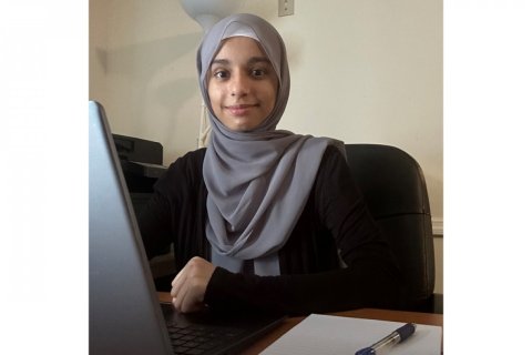 A person wearing a gray hijab works at a laptop while seated at a desk