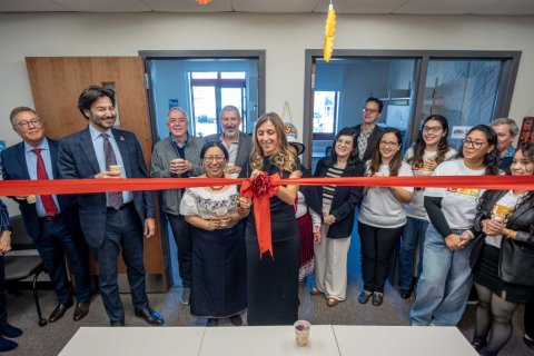 A woman cuts a large, red ribbon while a group of people watch
