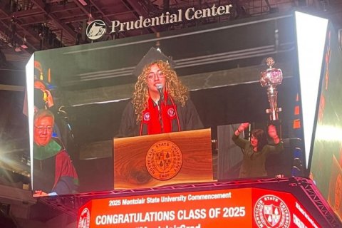 A college student speaks at graduation on a video board 