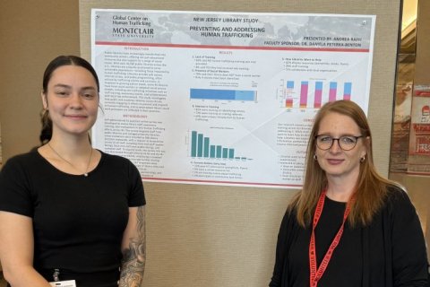 Two people pose in front of a printed presentation