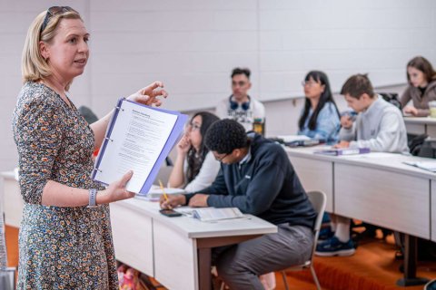 A college professor stands at the head of a class and delivers a lecture to students