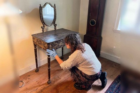 A person wearing gloves examines an old, wooden desk