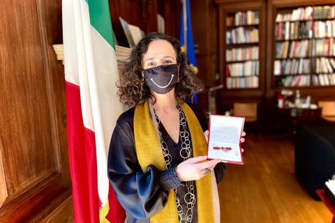 A woman stands in front of an Italian flag and holds open a display box 
