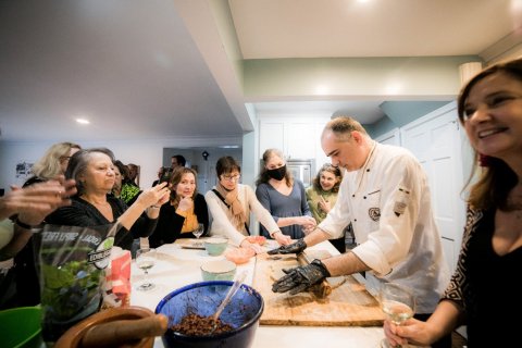 A chef rolls dough on a table while a group of people watch and take photos