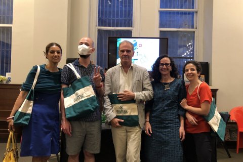 A group of people pose with tote bags in front of a small tv screen